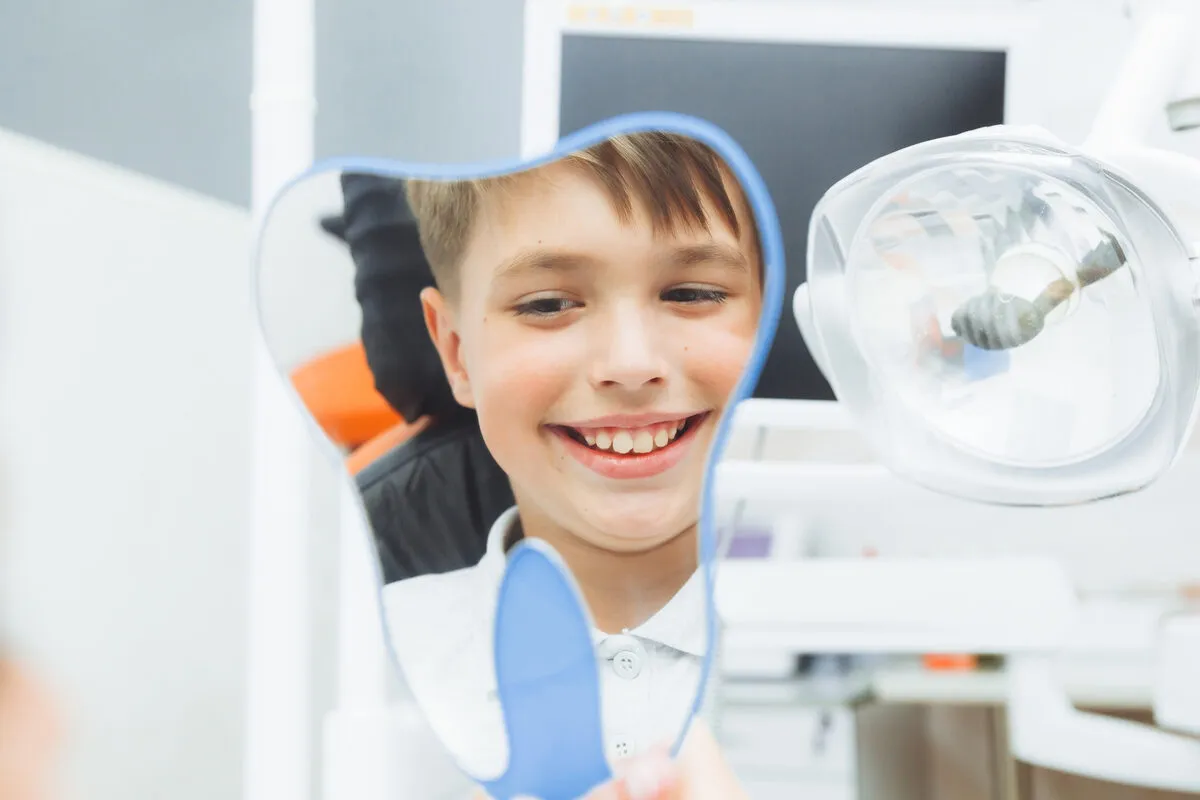 Boy smiling at his reflection in a dental mirror